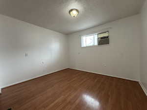 Empty room featuring wood finished floors, baseboards, a textured ceiling, and cooling unit