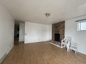 Unfurnished living room featuring light wood-type flooring, a textured ceiling, a brick fireplace, and baseboards