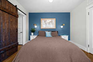 Bedroom with an accent wall, a barn door, wood finished floors, and baseboards