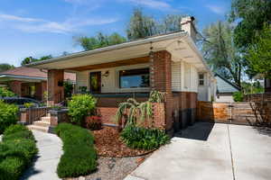 Bungalow-style house featuring brick siding, covered porch, a chimney, and fence