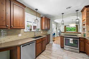 Kitchen with appliances with stainless steel finishes, a sink, backsplash, hanging light fixtures, and brown cabinets