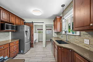 Kitchen with a sink, appliances with stainless steel finishes, a barn door, and tasteful backsplash