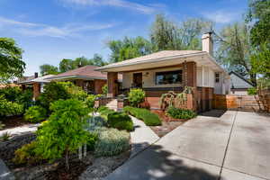 Bungalow-style house with brick siding, a chimney, fence, a gate, and a porch