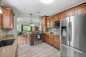Kitchen featuring stainless steel appliances, arched walkways, a sink, tasteful backsplash, and brown cabinetry