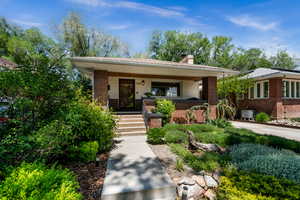 Bungalow-style house featuring central AC unit, brick siding, a porch, and a chimney