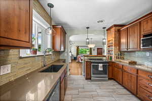 Kitchen with a sink, appliances with stainless steel finishes, backsplash, a peninsula, and brown cabinetry