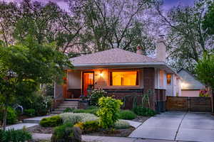 View of front of house featuring brick siding, a chimney, a porch, a gate, and fence