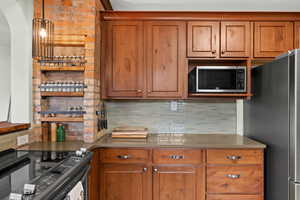 Kitchen with appliances with stainless steel finishes, brown cabinets, tasteful backsplash, and arched walkways
