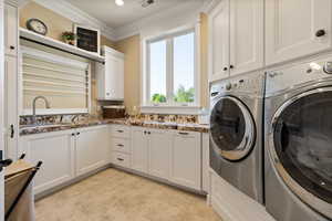 Washroom with cabinet space, washing machine and dryer, crown molding, and light tile patterned floors