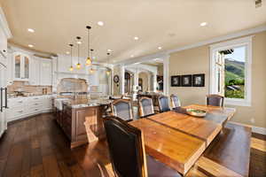 Dining room with decorative columns, arched walkways, dark wood-style flooring, recessed lighting, and crown molding