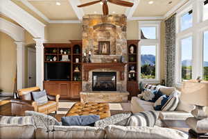 Living room featuring ornate columns, beamed ceiling, ceiling fan, a fireplace, and ornamental molding