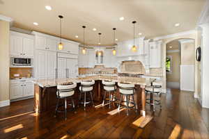 Kitchen with Sub-Zero fridge, stainless steel microwave, ornamental molding, arched walkways, white cabinets, and a large island