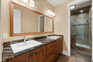 Full bathroom featuring a stall shower, double vanity, baseboards, and stone finish flooring