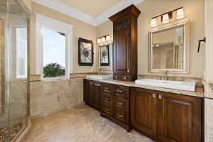 Bathroom with tile walls, tiled shower, crown molding, double vanity, and wainscoting