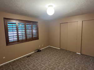 Unfurnished bedroom featuring a textured ceiling, baseboards, and multiple closets