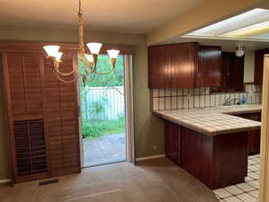 Kitchen featuring tile countertops, a chandelier, light carpet, and decorative backsplash