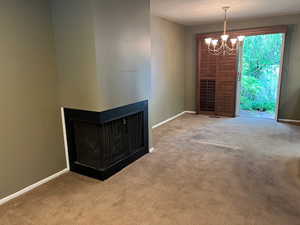 Unfurnished living room featuring carpet flooring, a chandelier, and baseboards