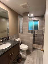 Full bathroom with tile walls, a tile shower, toilet, vanity, and tile patterned flooring