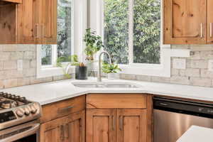 Kitchen with stainless steel appliances, a sink, brown cabinetry, light countertops, and backsplash