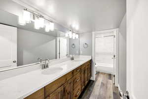 Full bath featuring wood finished floors, a textured ceiling, toilet, double vanity, and bathtub / shower combination