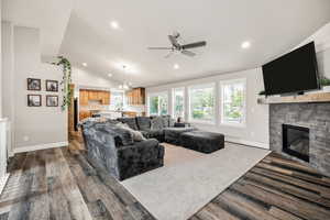 Living room featuring vaulted ceiling, a fireplace, dark wood-style floors, a ceiling fan, and recessed lighting
