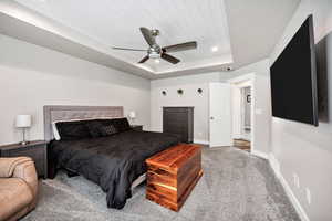 Carpeted bedroom featuring baseboards, a tray ceiling, ceiling fan, and recessed lighting