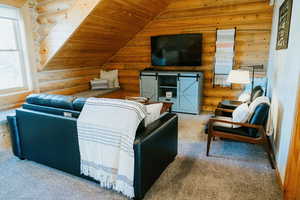 Carpeted living room featuring log walls, lofted ceiling, wooden ceiling, and a barn door