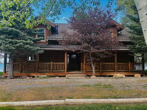 View of front of home with a shingled roof, log exterior, and covered porch