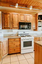 Kitchen featuring black microwave, white gas range oven, wood ceiling, and light tile patterned floors