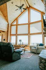 Carpeted living room featuring high vaulted ceiling, log walls, a ceiling fan, and wooden ceiling