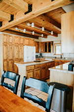 Kitchen featuring wood ceiling, beamed ceiling, white refrigerator with ice dispenser, light countertops, and tile patterned floors