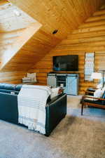 Carpeted living room featuring rustic walls, lofted ceiling, and wooden ceiling