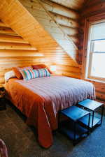 Carpeted bedroom with rustic walls and wooden ceiling
