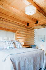 Bedroom with rustic walls, wooden ceiling, and beam ceiling