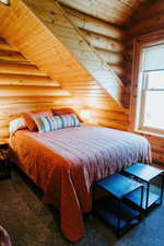 Bedroom with rustic walls, wood ceiling, and carpet floors