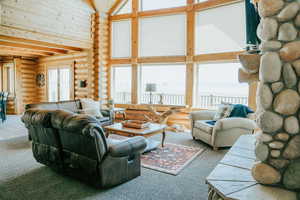 Living room featuring high vaulted ceiling, rustic walls, carpet flooring, and beam ceiling