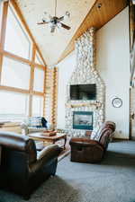 Living area featuring wooden ceiling, high vaulted ceiling, a stone fireplace, carpet flooring, and a ceiling fan