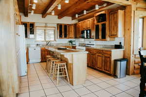 Kitchen with white appliances, wood ceiling, a kitchen bar, light countertops, and brown cabinetry