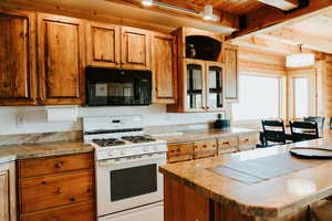 Kitchen featuring black microwave, white gas range oven, wooden ceiling, beamed ceiling, and brown cabinets