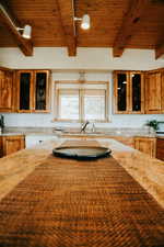 Kitchen featuring a sink, wood ceiling, beamed ceiling, light stone countertops, and glass insert cabinets