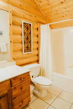 Bathroom with log walls, tile patterned floors, toilet, vanity, and shower / tub combo