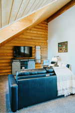 Carpeted living room featuring log walls and beamed ceiling