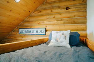 Bedroom featuring rustic walls, wooden ceiling, and lofted ceiling