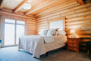 Bedroom with wood ceiling, rustic walls, carpet flooring, beamed ceiling, and access to exterior