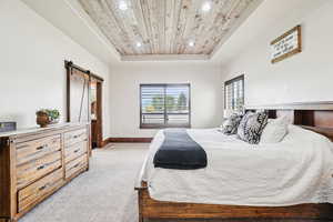 Bedroom with a barn door, a raised ceiling, light carpet, wooden ceiling, and recessed lighting