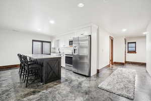 Kitchen with appliances with stainless steel finishes, finished concrete flooring, baseboards, a kitchen island, and white cabinetry
