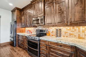 Kitchen featuring stainless steel appliances, baseboards, light stone counters, wood finished floors, and tasteful backsplash