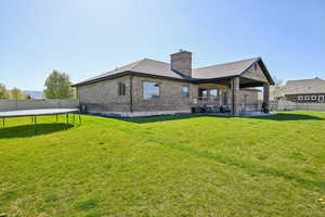 Back of house with a trampoline, brick siding, a chimney, a patio, and a shingled roof