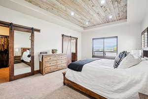Carpeted bedroom with a barn door, a raised ceiling, wood ceiling, recessed lighting, and a spacious closet