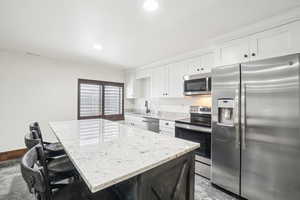 Kitchen featuring appliances with stainless steel finishes, white cabinets, a center island, a sink, and recessed lighting